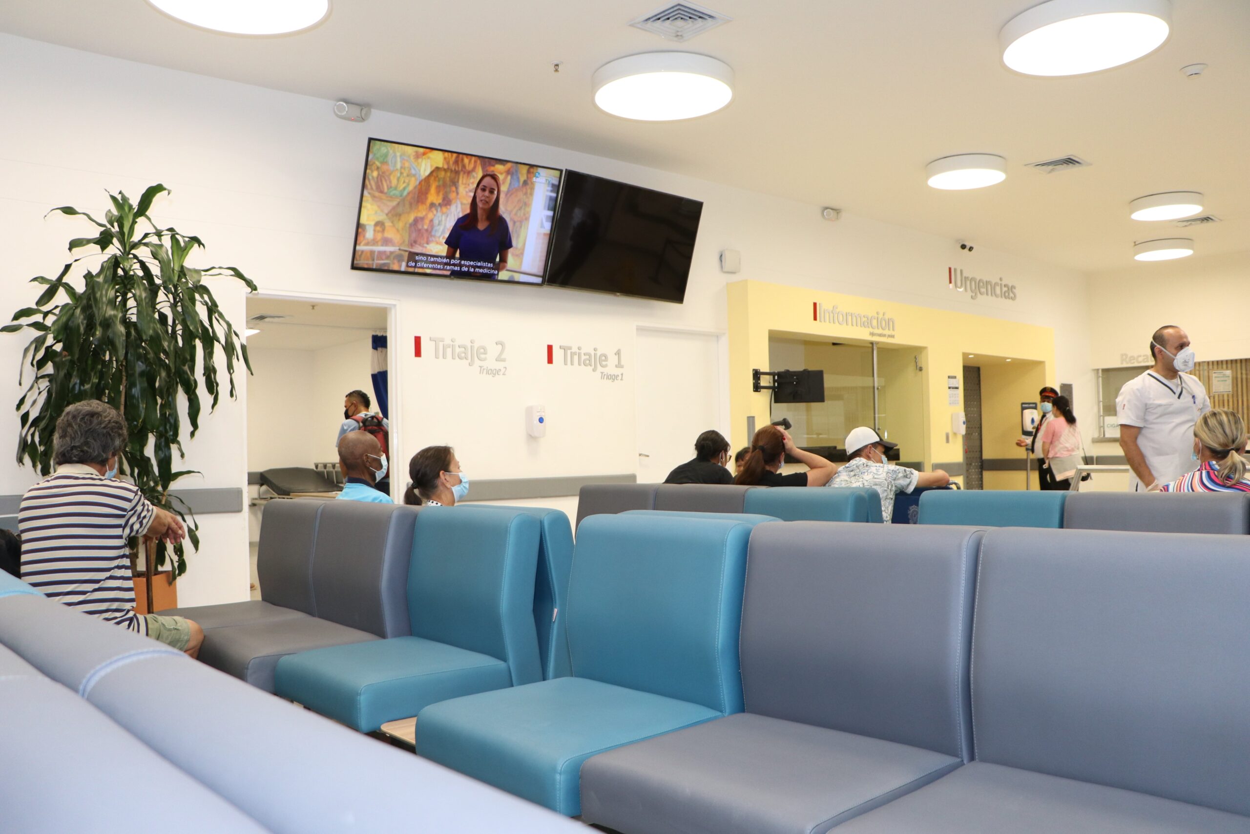 Instalaciones internas del área de urgencias, personas caminando y personas sentadas.
